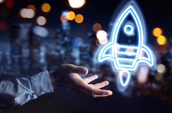 A hand is reaching out towards a glowing blue rocket icon, symbolizing innovation and potential. The background features blurred lights that suggest a futuristic cityscape at night.