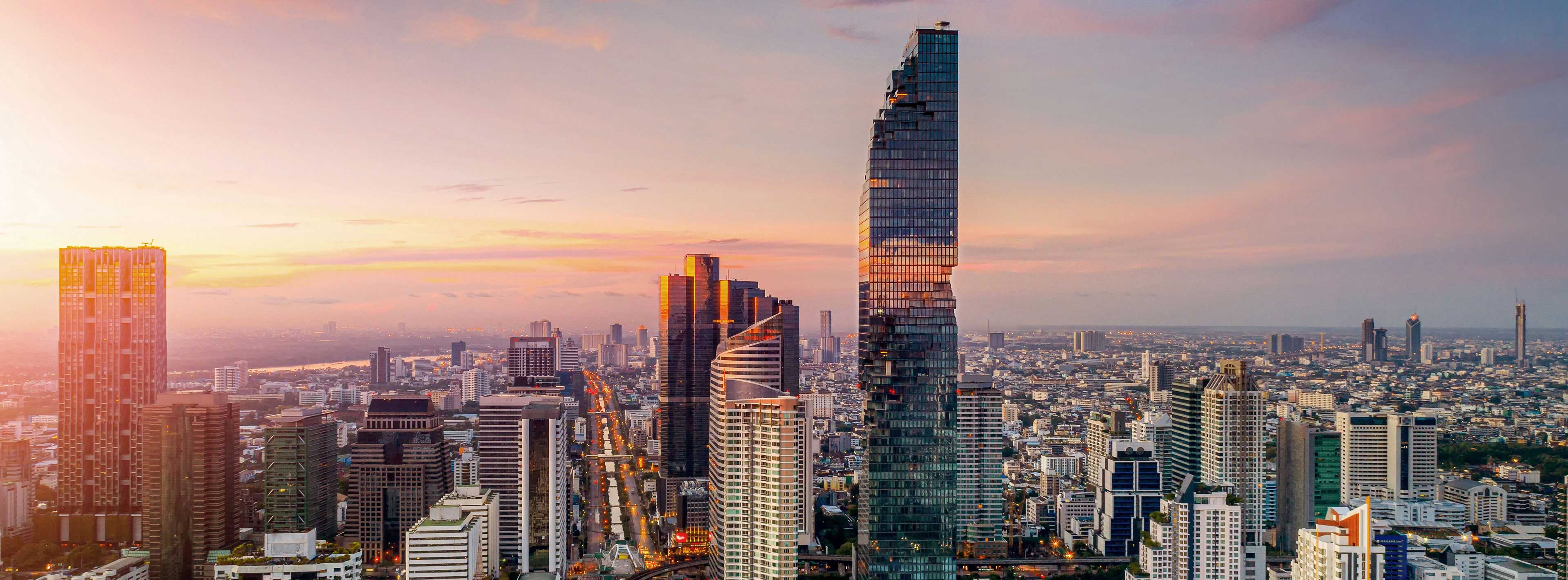 Eine Skyline mit modernen Wolkenkratzern bei Sonnenuntergang. Im Vordergrund sind hohe Gebäude sichtbar, darunter ein markanter, spiralförmiger Turm. Der Himmel ist in sanften Rosa- und Orangetönen gefärbt, was eine stimmungsvolle Atmosphäre erzeugt.