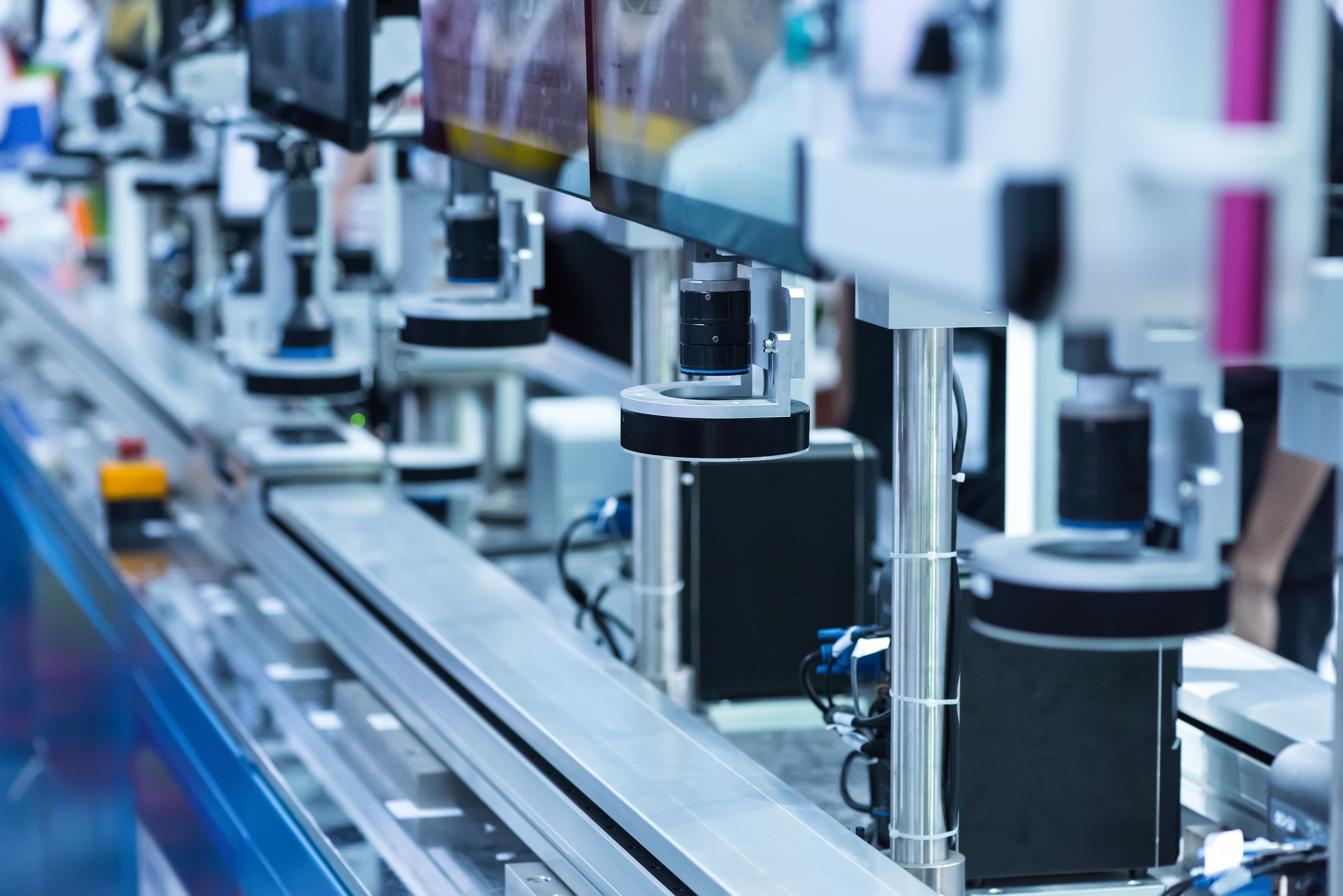 A close-up view of a production line featuring multiple robotic arms with cameras mounted on flexible stands. The machines are aligned along a conveyor belt, which is part of a high-tech manufacturing environment.