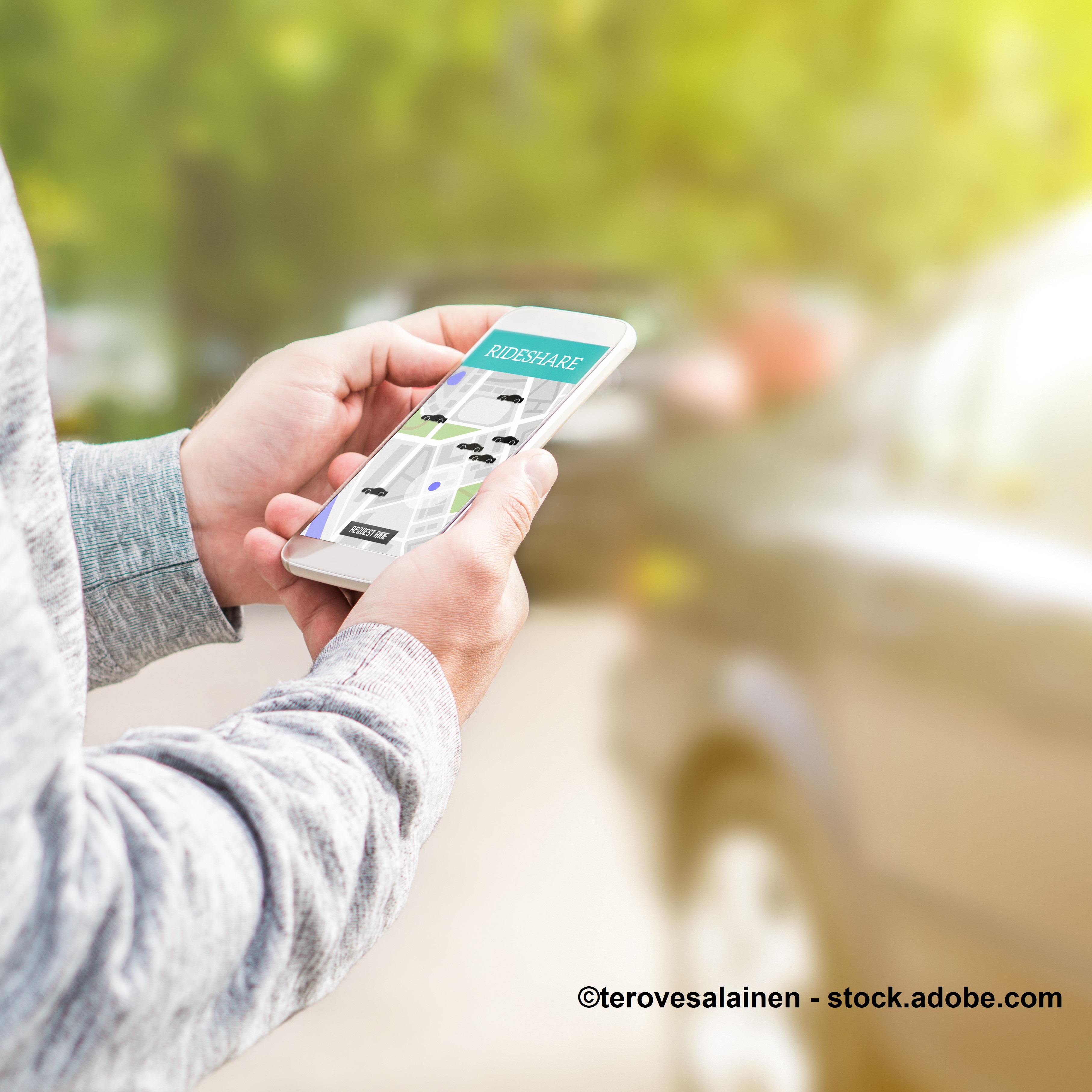 Eine Person hält ein Smartphone in der Hand, auf dem eine Rideshare-App angezeigt wird. Die App zeigt eine Karte mit Fahrzeugen in der Umgebung. Im Hintergrund sind unscharf parkende Autos zu erkennen.