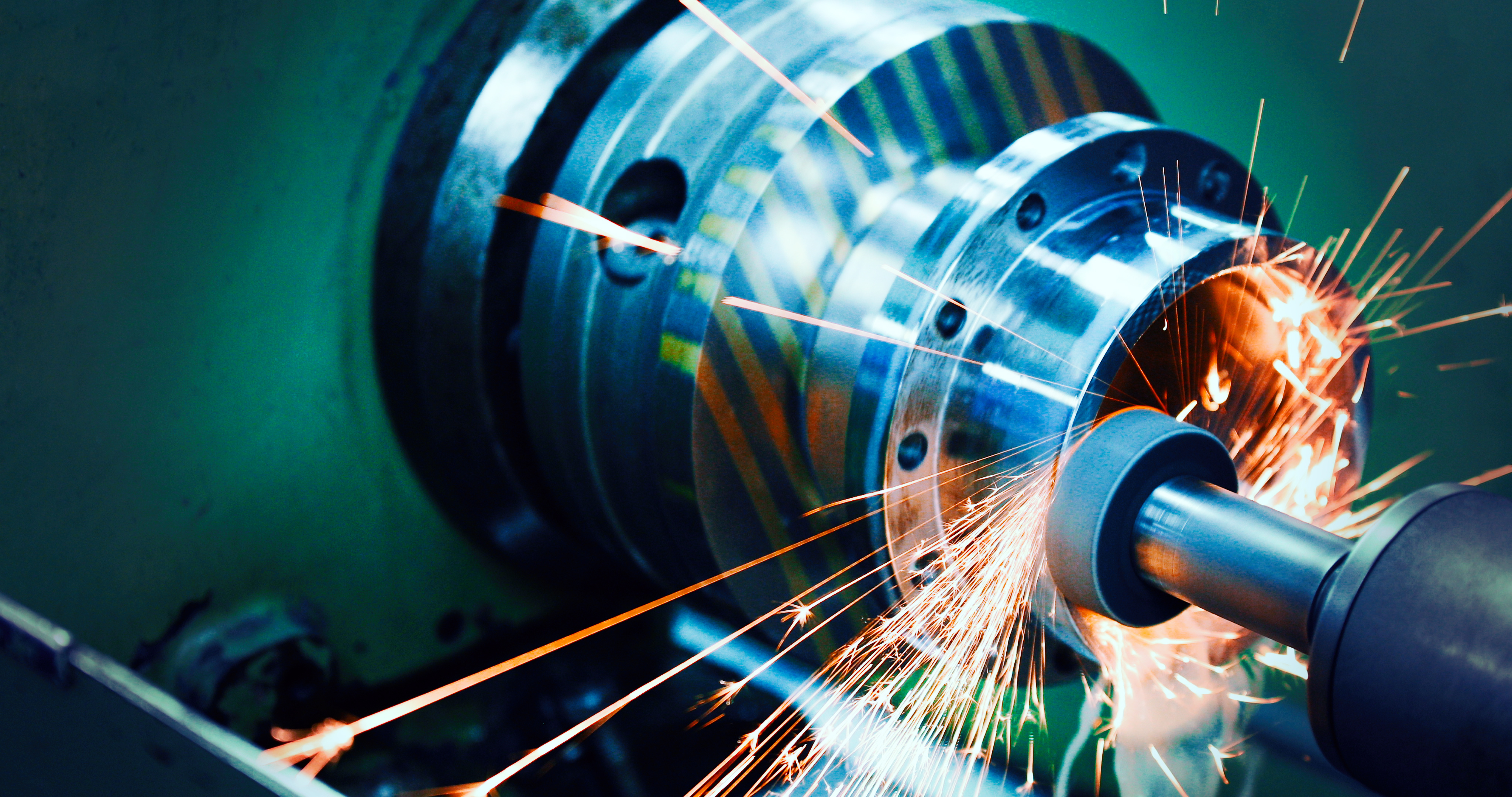 A close-up view of a metalworking lathe in operation, producing sparks as a cylindrical metal piece is being shaped. The image highlights the tools and swirling motion, emphasizing the process of precision machining in a workshop.