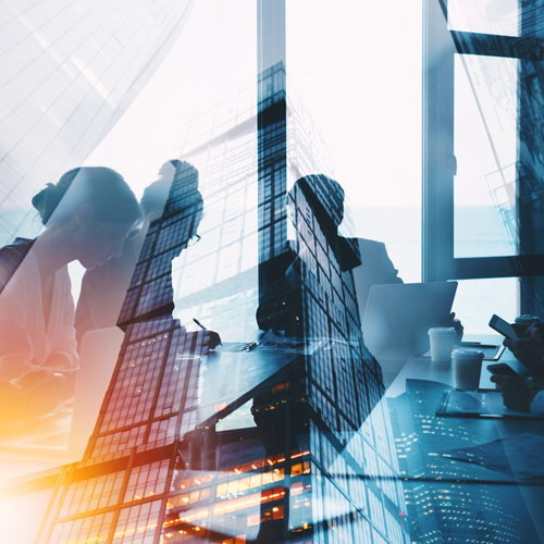 Die Abbildung zeigt eine Besprechung in einem modernen Büro. Mehrere Personen sind an einem Tisch versammelt und arbeiten an Laptops, während große Fenster Blick auf eine Stadtlandschaft bieten. Die Silhouetten der Gebäude sind im Vordergrund zu sehen, was eine doppelte Belichtung erzeugt.