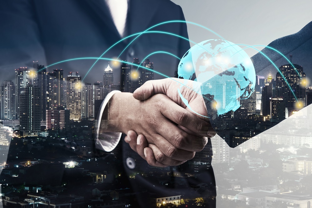 A close-up of two hands shaking in a business agreement, with a digital globe overlay and lines representing connections. The background features a city skyline at dusk, symbolizing global business and networking opportunities.