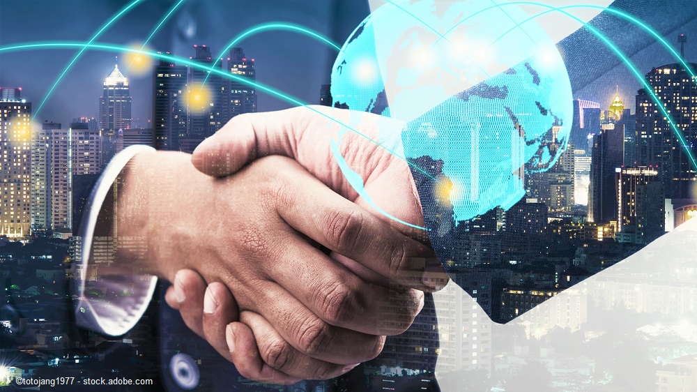 Two hands are shaking in a business setting, symbolizing partnership and collaboration. Behind them, a digital globe and a city skyline suggest a global connection and modern technology. The image conveys themes of international business and teamwork.