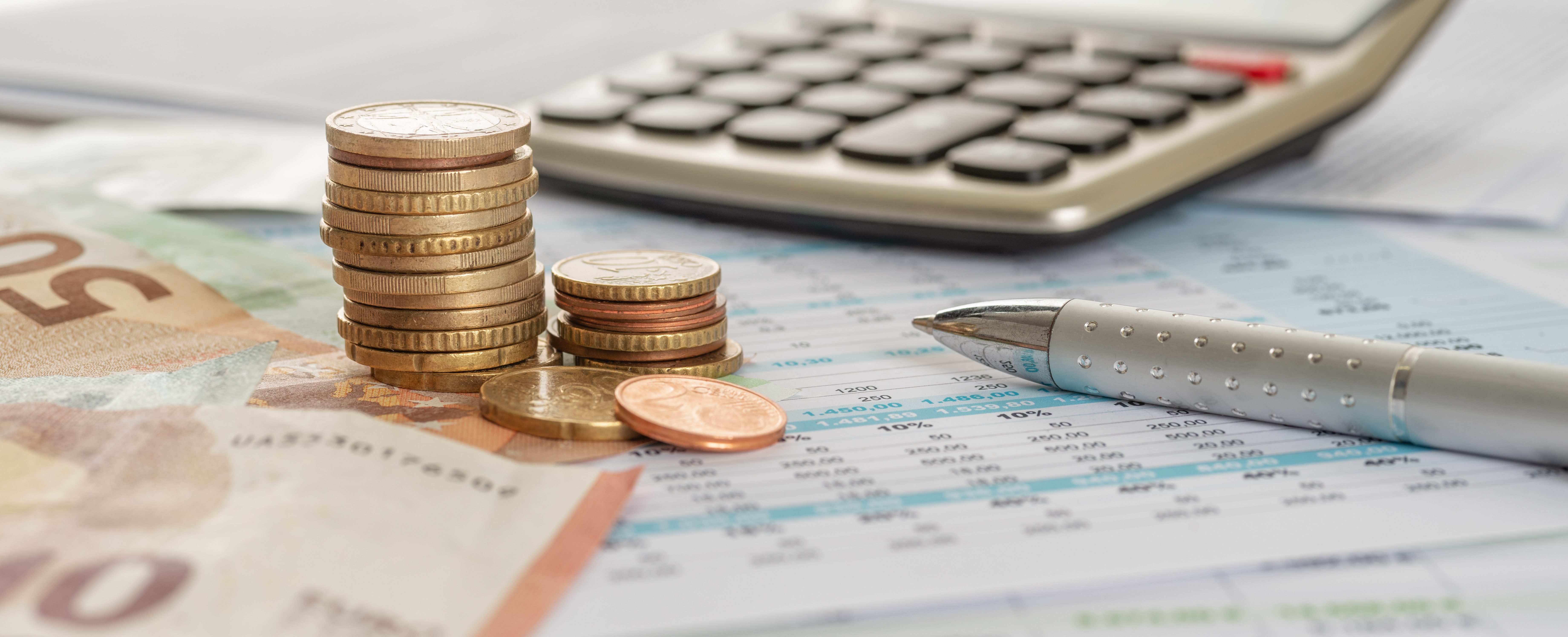 A stack of Euro coins is positioned on a financial report, accompanied by a pen and a calculator. The background features various Euro banknotes, suggesting a theme of budgeting or financial management. The overall setting conveys a focus on personal finance and accounting.