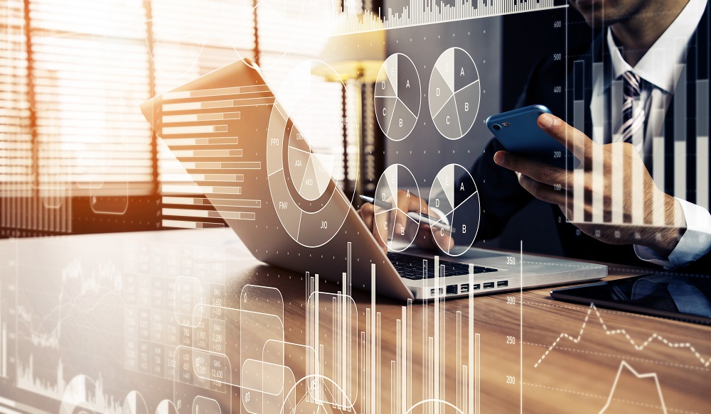 A close-up of a person in business attire, working on a laptop while holding a smartphone. Data visualization graphs, including pie charts and bar graphs, overlay the scene, illustrating a focus on analytics and business strategy in a professional setting.
