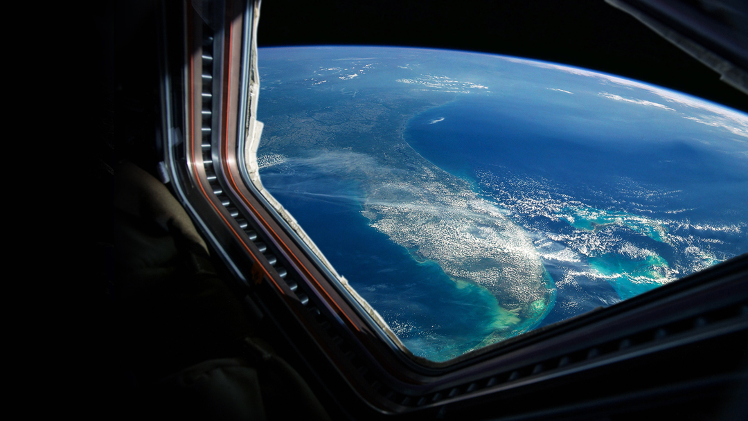 A view of Earth from space is seen through a spacecraft window. The image shows a curved horizon with land, clouds, and vast blue oceans, highlighting the planet's natural beauty in a serene atmosphere.