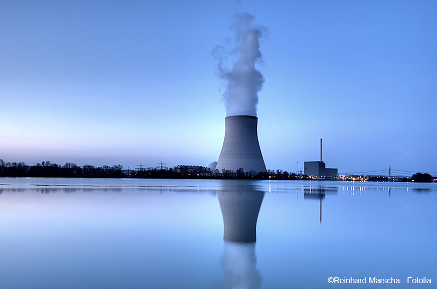 A cooling tower of a nuclear power plant stands near a calm body of water at dusk. Steam rises from the tower, reflecting in the water's surface. The sky transitions from blue to twilight, creating a serene yet industrial landscape.