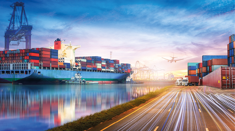 Ein großer Containerschiff im Hafen, beladen mit zahlreichen bunter Container. Im Hintergrund sind Kräne und Containerlager sichtbar, während ein Flugzeug über den Hafen fliegt. Das Wasser spiegelt die Farben des Himmels wider, während eine Straße neben dem Hafen verläuft.