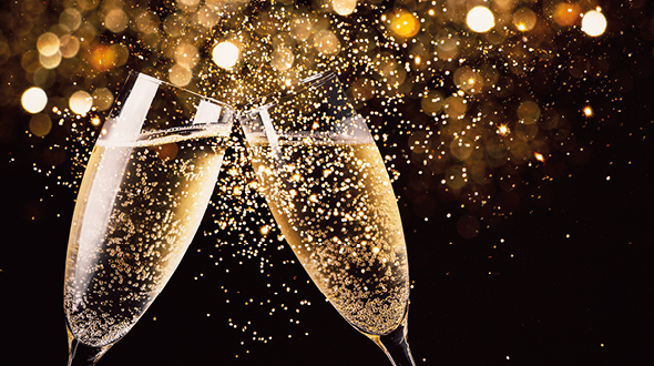 Zwei Sektgläser stoßen an und sind gefüllt mit sprudelndem Getränk. Im Hintergrund funkeln goldene Lichter, was eine festliche Atmosphäre schafft.