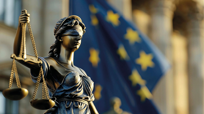 Eine Statue der Justitia, die eine Augenbinde trägt und eine Waage in der rechten Hand hält, symbolisiert Gerechtigkeit und Unparteilichkeit. Im Hintergrund weht eine europäische Flagge, die die Verbindung zur Europäischen Union verdeutlicht.