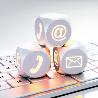 Drei Würfel mit Symbolen für Kommunikationsmethoden sind auf einer Tastatur gestapelt. Die Symbole zeigen Telefon, E-Mail und @-Zeichen. Die Würfel sind hell erleuchtet und heben sich vom Hintergrund ab, was die verschiedenen Kernarten der digitalen Kommunikation darstellt.