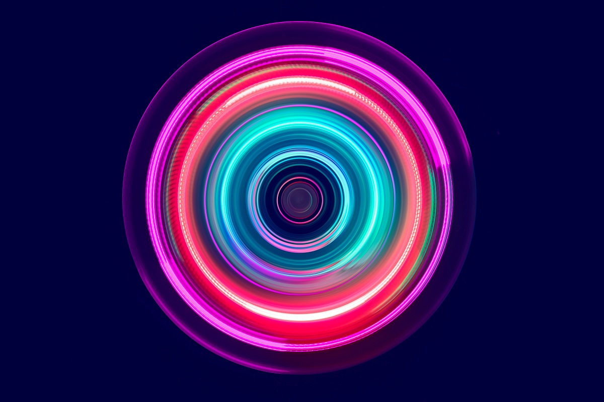Ein leuchtender, kreisförmiger Lichtwirbel mit intensiven Farben in Blau, Pink und Lila, der spiralförmig ansteigt. Die leuchtenden Ränder wirken dynamisch und vermitteln ein Gefühl von Bewegung und Energie. Der Hintergrund ist dunkel, wodurch die Farben stärker zur Geltung kommen.