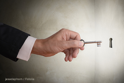 Ein Mann hält einen Schlüssel in der Hand und steht vor einem Schlüsselloch in einer Wand. Die Szene vermittelt das Gefühl von Zugang oder Entdeckung.