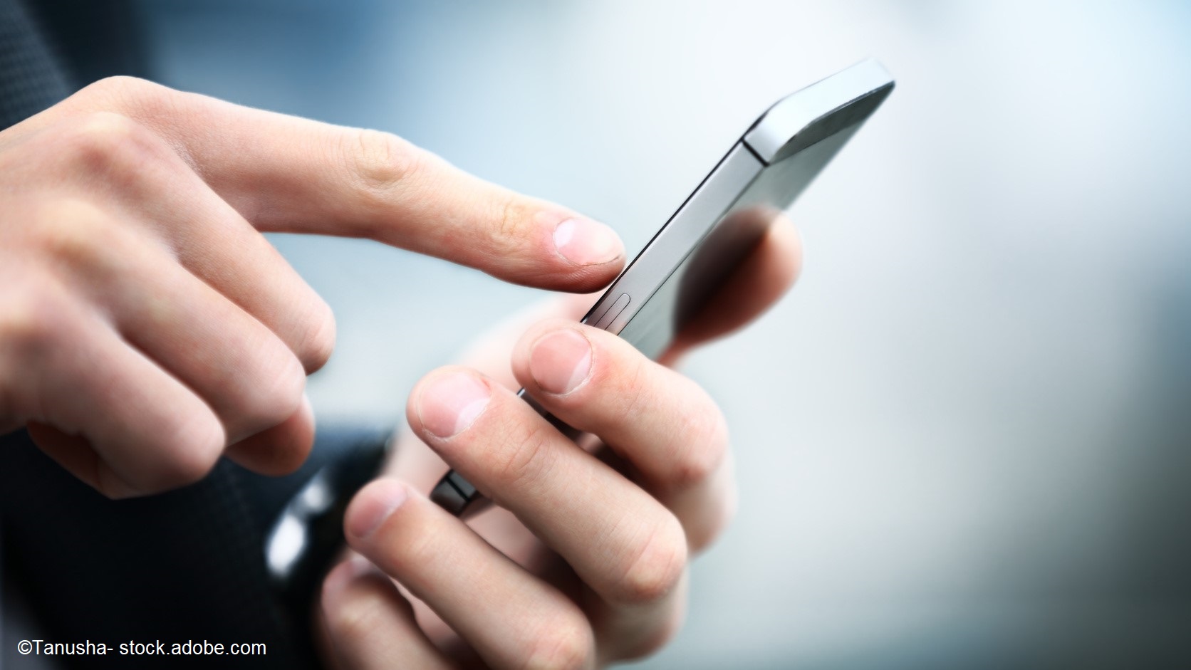 A close-up of a person's hand holding a smartphone, with a finger poised to touch the screen. The background is softly blurred, emphasizing the action of using the device.