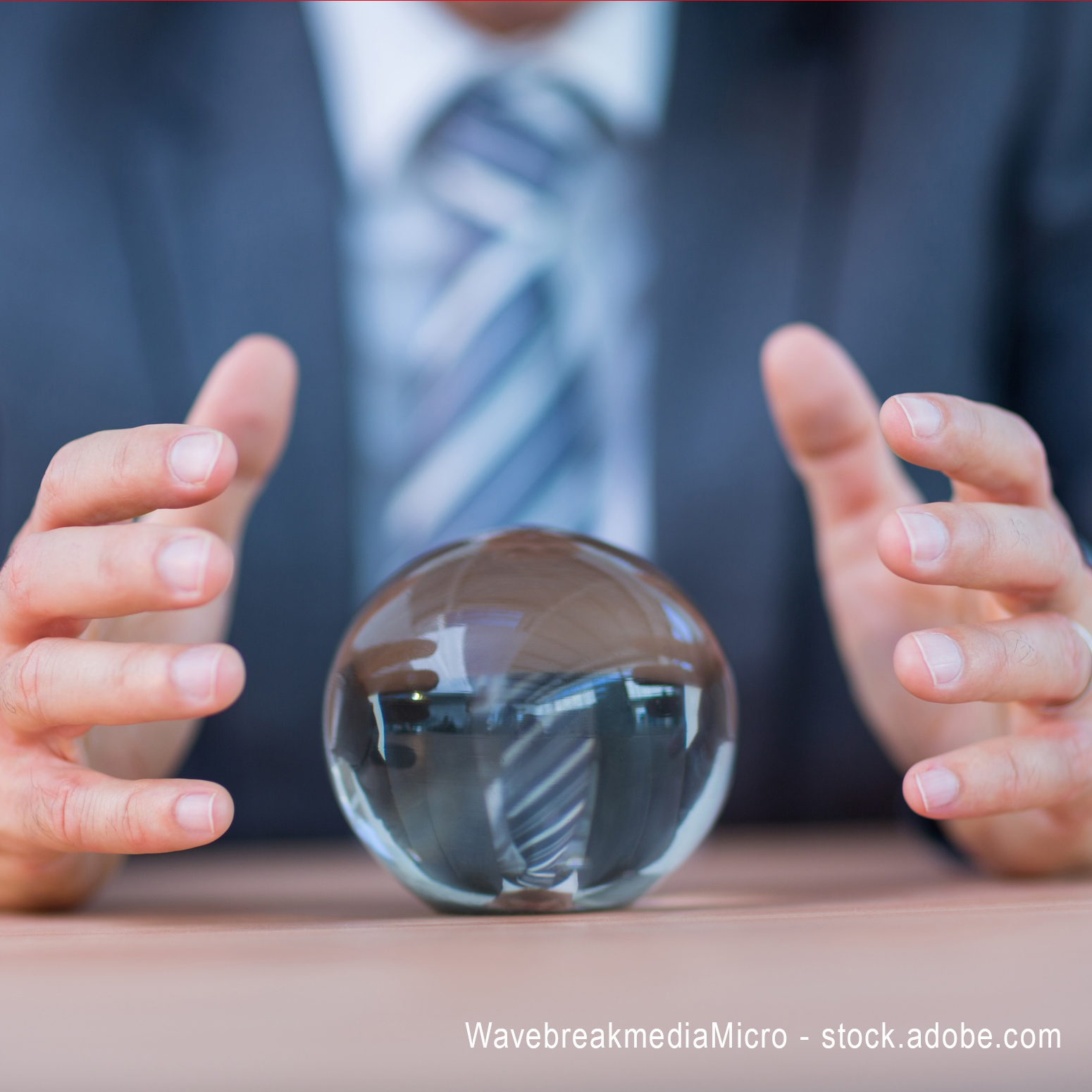 Ein Mann in Anzug sitzt an einem Tisch und beugt sich über eine Kristallkugel. Seine Hände sind schützend um die Kugel platziert, was auf eine mystische oder beratende Atmosphäre hinweist. Der Hintergrund ist unscharf und hebt die Kugel hervor.