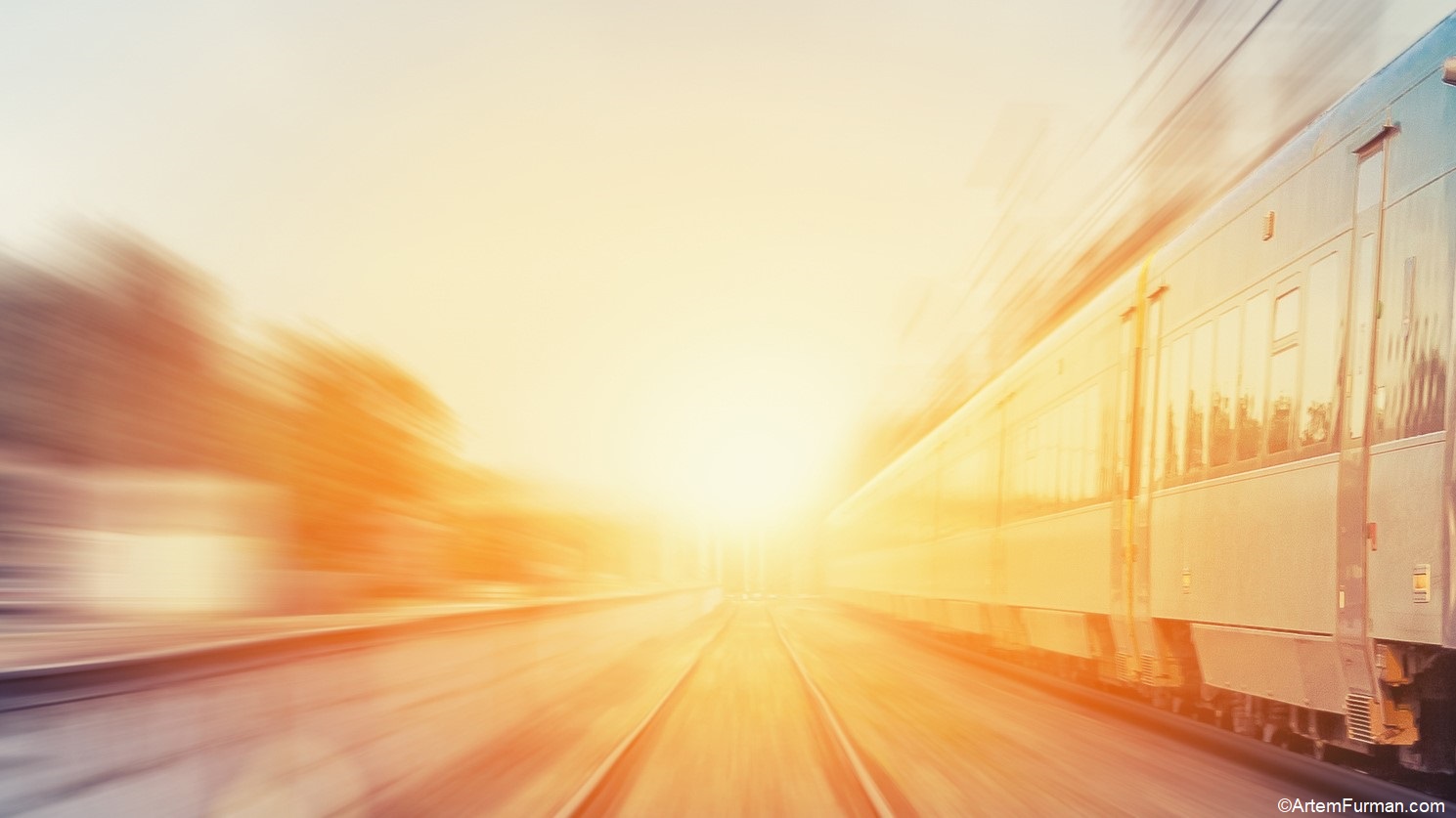 A blurred image of a speeding train, set against a bright sunrise backdrop. The scene conveys a sense of motion and direction, highlighting the tracks and the warm glow of the sun. The atmosphere suggests early morning travel and anticipation.