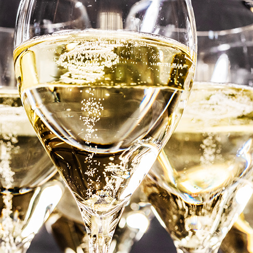 Die Abbildung zeigt mehrere Gläser mit sprudelndem, blassem Getränk, das wie Sekt oder Champagner aussieht. Die Bläschen steigen im Glas auf und reflektieren Licht, was eine festliche Stimmung vermittelt. Der Hintergrund ist unscharf und hebt die Gläser hervor.