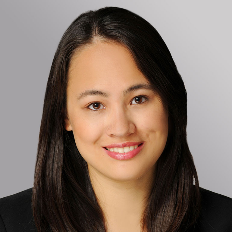 Porträt einer Frau mit langen, dunklen Haaren und einem freundlichen Lächeln. Sie trägt einen schwarzen Blazer. Der Hintergrund ist hell und neutral gehalten.