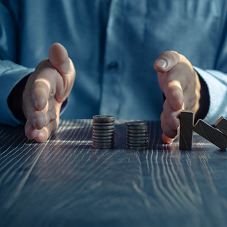 Ein Mann mit einem blauen Hemd steht an einem Tisch und hält seine Hände in einer abwehrenden Position. Vor ihm befinden sich zwei Stapel Münzen, die durch ein Holzzeichen „W“ getrennt sind. Das Bild vermittelt eine Botschaft über finanzielle Entscheidungen oder Strategien.