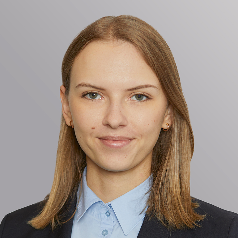 Porträt einer lächelnden Frau mit blonden, schulterlangen Haaren. Sie trägt einen dunklen Blazer und ein hellblaues Hemd. Der Hintergrund ist neutral und unauffällig.