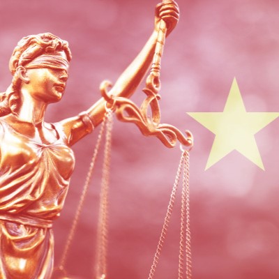 Eine goldene Statue der Justitia, die eine Waage in der rechten Hand hält und ein Schwert in der linken. Ihre Augen sind verbunden, was Unparteilichkeit symbolisiert. Im Hintergrund ist ein verschwommenes Sternsymbol zu sehen.