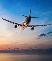 Ein Flugzeug hebt in den Abendhimmel ab, umgeben von einem warmen, orangefarbenen Sonnenuntergang. Der Himmel ist klar und es sind einige Wolken sichtbar. Das Bild vermittelt ein Gefühl von Freiheit und Reisen.