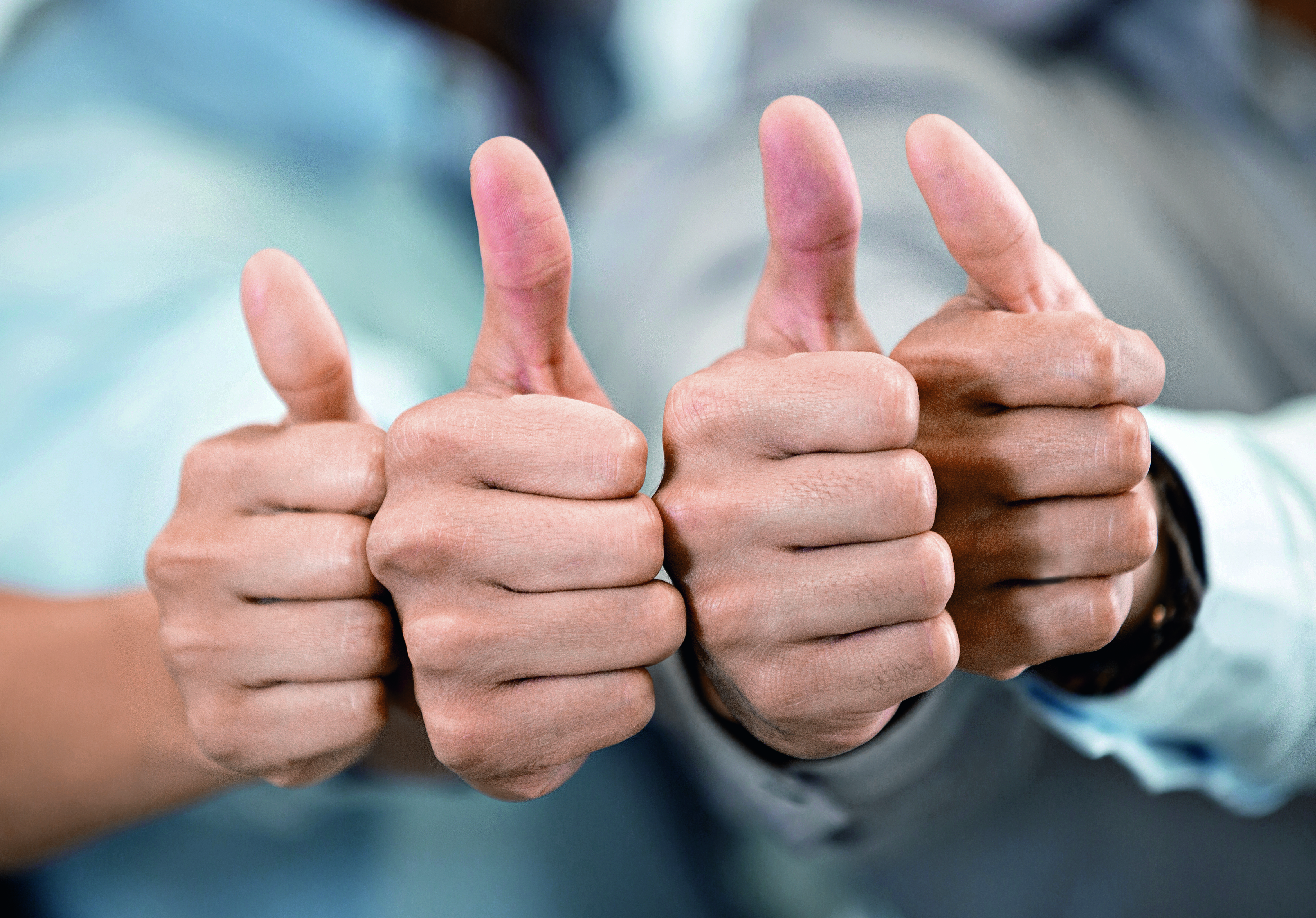 Vier Hände zeigen Daumen hoch, was Zustimmung oder Anerkennung symbolisiert. Die Hände sind auf gleicher Höhe angeordnet, mit den Daumen, die prominent in die Höhe zeigen.
