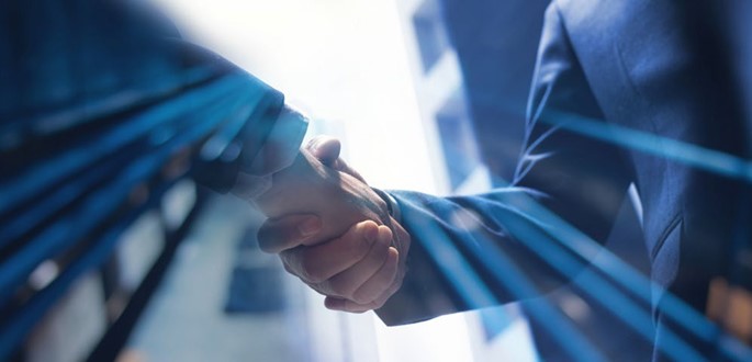 Zwei Hände schütteln sich, symbolisieren eine Vereinbarung oder Kooperation. Die Umgebung ist verschwommen, mit einem modernen, hellen Hintergrund. Das Bild strahlt Professionalität und Partnerschaft aus.