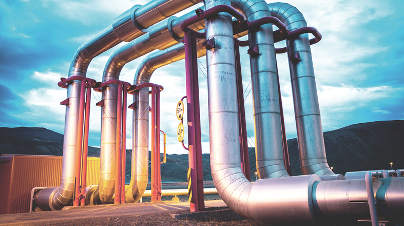 Das Bild zeigt eine Gruppe von großen, metallischen Rohren, die an einem industriellen Standort installiert sind. Die Rohre sind unterschiedlich geformt und haben rote Verbindungen. Im Hintergrund ist eine wolkige Landschaft zu sehen, die eine gedämpfte Beleuchtung erzeugt.