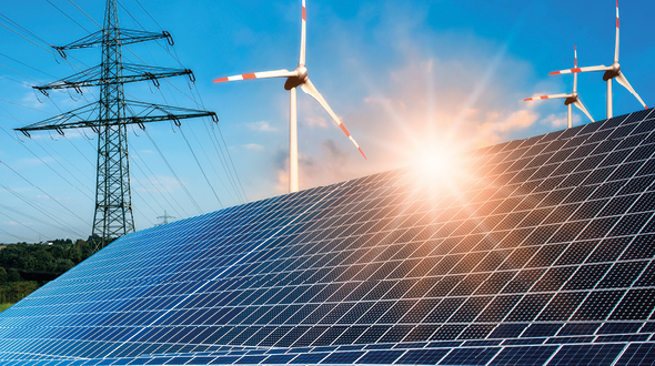 Das Bild zeigt Solarpanels im Vordergrund, die im Sonnenlicht glänzen. Im Hintergrund sind Windkraftanlagen zu sehen, die sich gegen einen blauen Himmel abheben. Diese Darstellung symbolisiert erneuerbare Energien und nachhaltige Technologien.