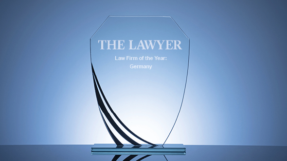Eine transparente Auszeichnung in Form eines Schildes mit der Aufschrift „THE LAWYER“ und „Law Firm of the Year: Germany“. Die Trophäe hat eine elegante, geschwungene Basis und reflektiert das Licht, was ihr ein prestigeträchtiges Aussehen verleiht.