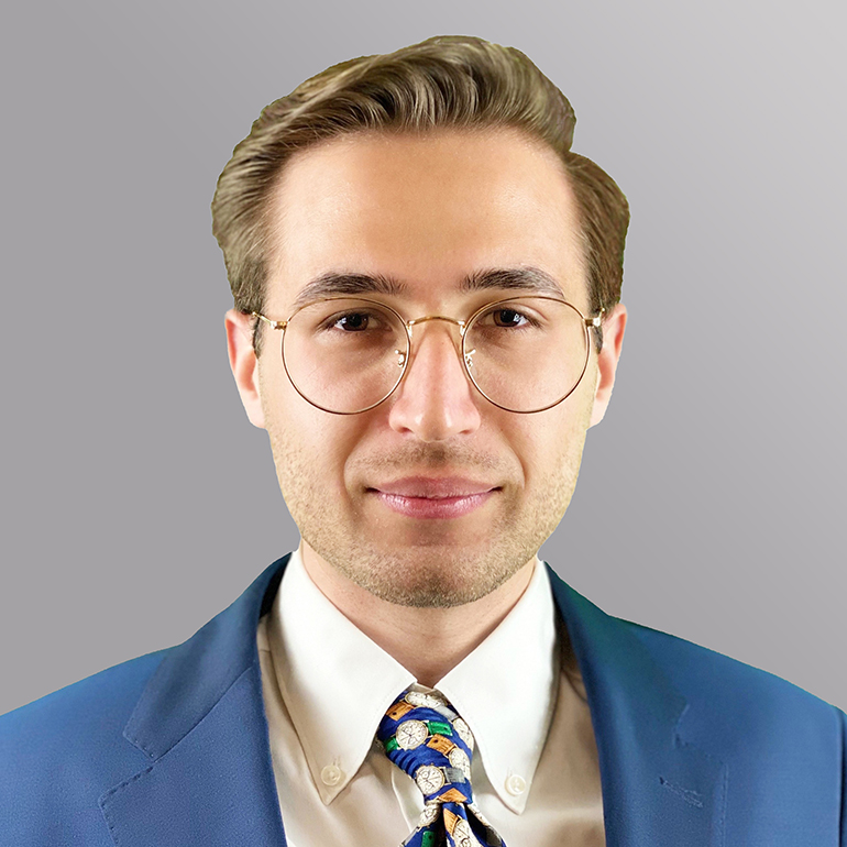 Ein junger Mann mit blonden, nach hinten gekämmten Haaren und einer hellen Bluse trägt eine blaue Jacke und eine auffällige, gemusterte Krawatte. Er blickt direkt in die Kamera, mit einer neutralen Miene, vor einem grauen Hintergrund.