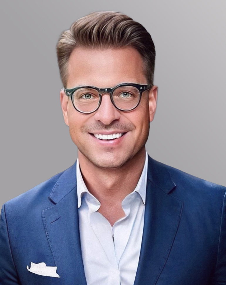 Porträt eines lächelnden Mannes mit modernen Brillen und mittellangen, stylishen Haaren. Er trägt einen blauen Anzug und ein helles Hemd. Der Hintergrund ist einfarbig grau.