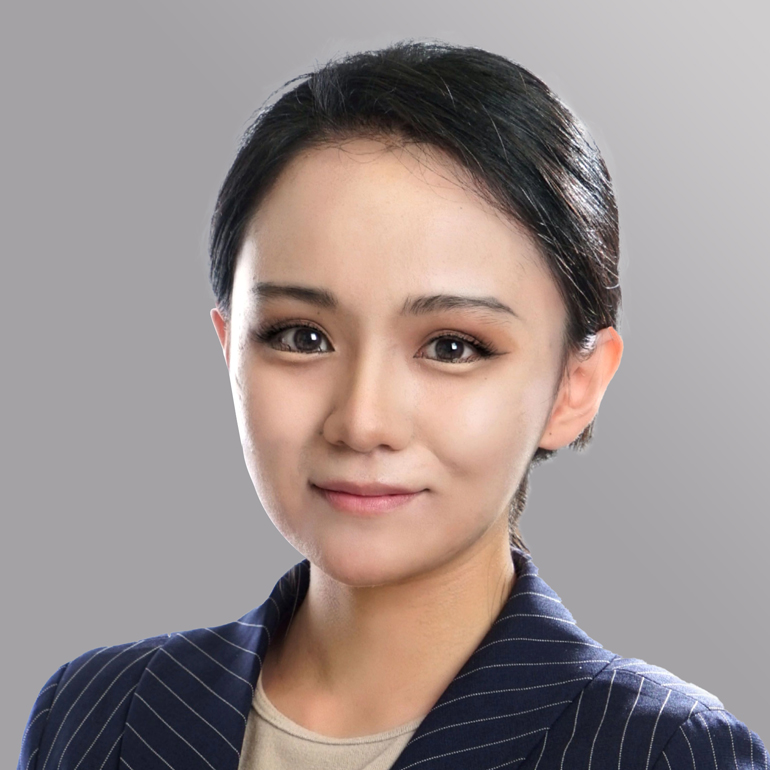 Ein Porträt einer Frau mit dunklem Haar, die einen Blazer mit feinen Streifen trägt. Sie hat ein freundliches Lächeln und schaut direkt in die Kamera. Der Hintergrund ist einfarbig und unscharf.