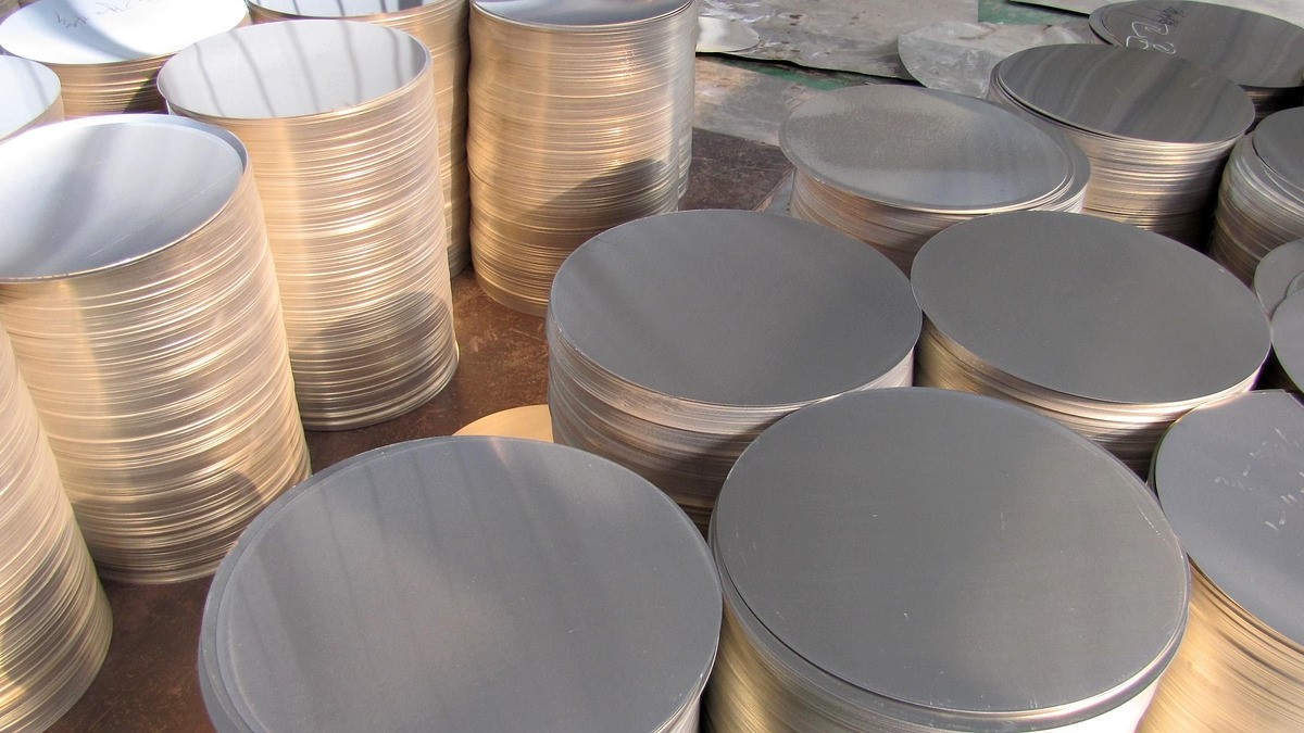 A collection of shiny, circular metal discs stacked vertically. The discs vary slightly in size and are positioned closely together, creating a layered effect. The metallic surface reflects light, emphasizing their smooth and uniform appearance. This arrangement suggests they are ready for industrial use or manufacturing.