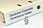A binder titled "Deutscher Corporate Governance Kodex" is displayed, featuring the text prominently on the spine. In front of the binder, a silver section symbol (§) is positioned, indicating a reference to legal or regulatory content related to corporate governance.