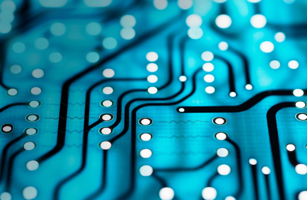 Nahaufnahme einer Leiterplatte mit blauen Hintergrund und schwarzen Leiterbahnen. Auf der Fläche sind weiße Kontaktpunkte angeordnet, die verschiedene elektronische Verbindungen darstellen. Die Komposition vermittelt ein technologisches und modernes Gefühl.