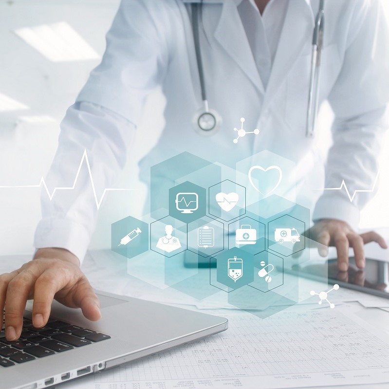 A healthcare professional in a lab coat is using a laptop, with a stethoscope around their neck. In the foreground, digital icons representing healthcare elements, including a heart, medical tools, and patient data, are displayed, symbolizing the integration of technology in medical practice.