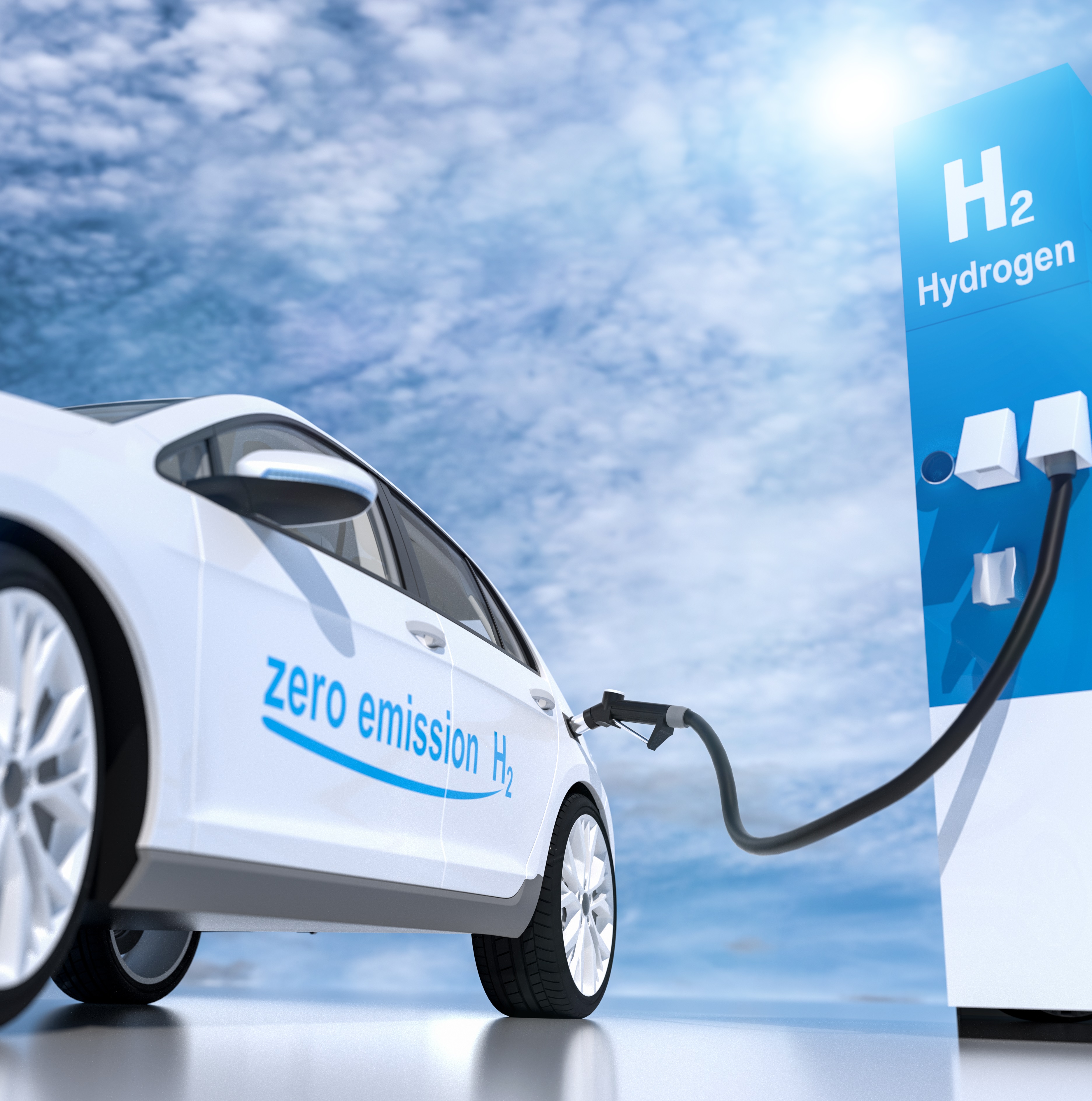 Ein Wasserstoffauto wird an einer Betankungsstation aufgeladen. Das Fahrzeug trägt die Beschriftung „zero emission H₂“, was auf den emissionsfreien Betrieb hinweist. Im Hintergrund ist ein blauer Himmel mit einigen Wolken zu sehen.