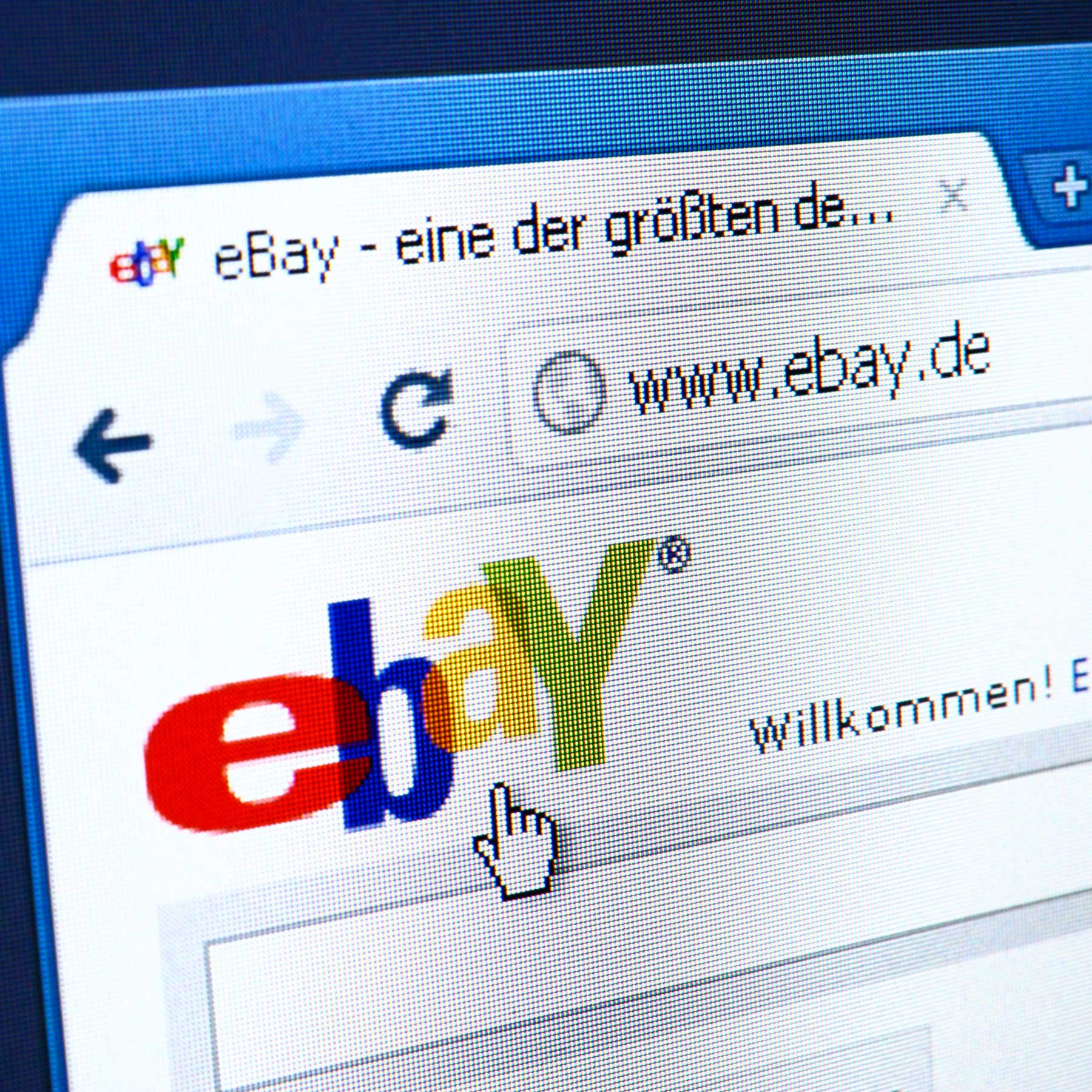 The image displays a close-up of a computer screen featuring the eBay logo in colorful text. A cursor is positioned near the logo, indicating user interaction. The webpage suggests a welcome message, indicating that it is an eBay homepage.