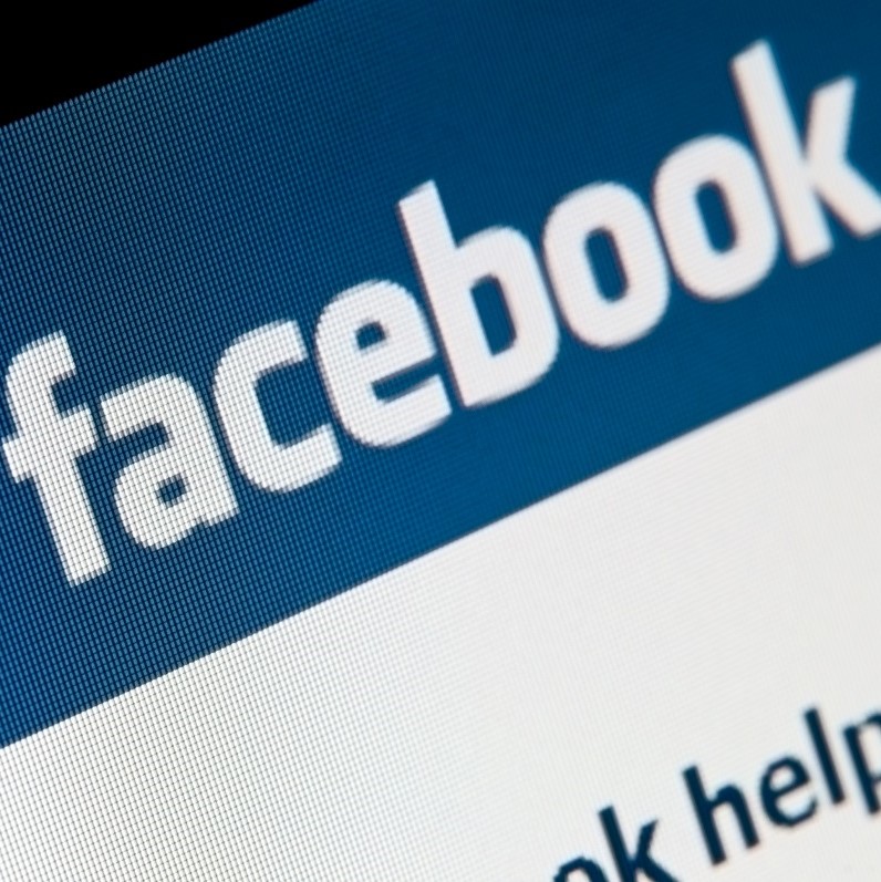 The image features a close-up of the Facebook logo displayed on a digital screen, with the word "facebook" prominently visible in white text against a blue background. The logo conveys a sense of social connectivity and online interaction.