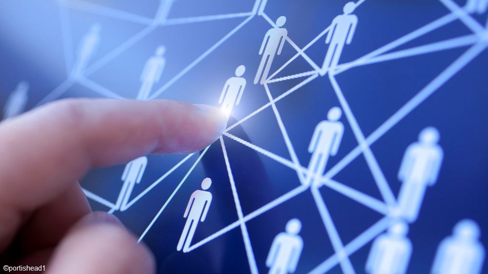 A close-up of a hand pointing at a glowing connection on a digital network of simplified human figures representing connections, symbolizing communication or networking. The background is dark, enhancing the focus on the interactive elements of the network.