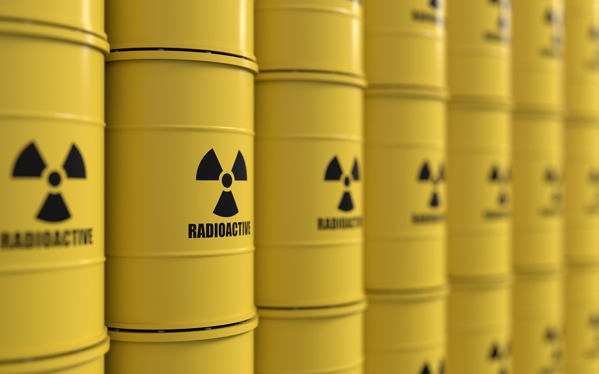 A series of yellow barrels labeled "RADIOACTIVE" are stacked closely together, featuring a black radiation symbol on each barrel. The image emphasizes the containment of hazardous materials.