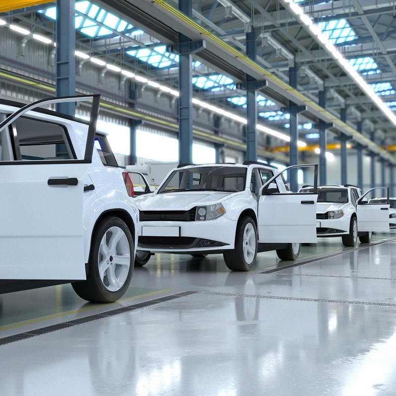 A row of several white cars is parked in a spacious automotive factory. The doors of each car are open, suggesting they are being prepared for inspection or assembly. Bright overhead lights illuminate the clean, polished floor.
