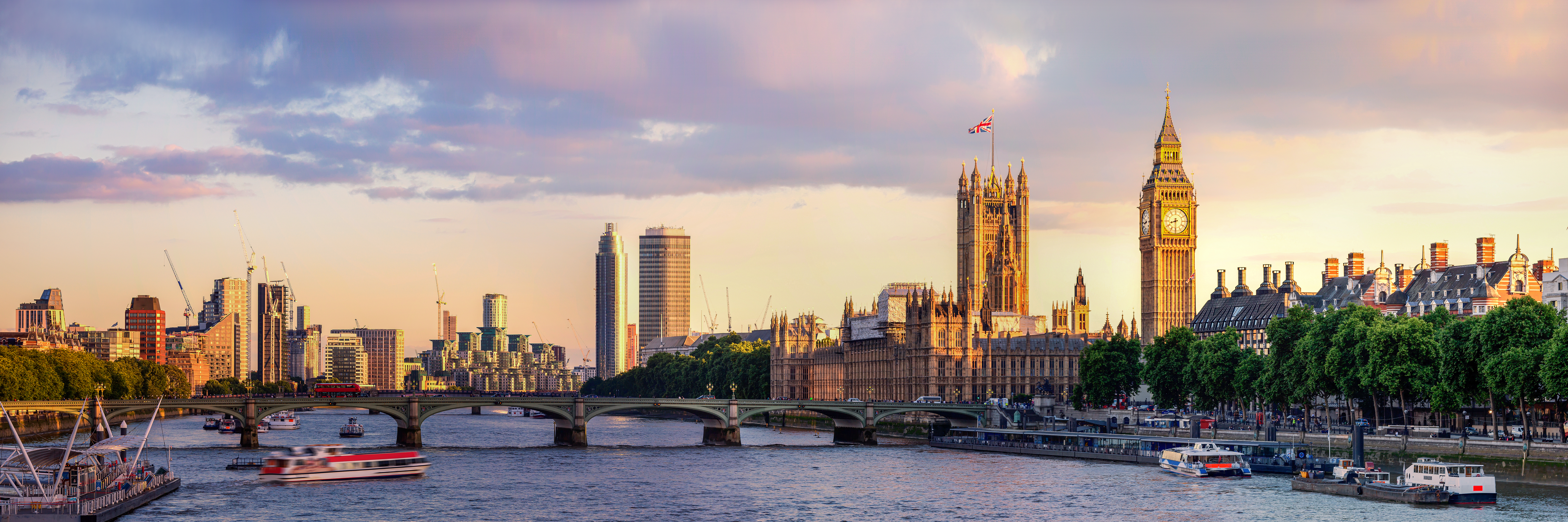 Panorama von London mit der Themse im Vordergrund. Auf der rechten Seite sind das Parlamentsgebäude und der Uhrturm, bekannt als Big Ben. Im Hintergrund sind moderne Wolkenkratzer zu sehen, während im Wasser Boote fahren. Der Himmel zeigt sanfte Pastellfarben.