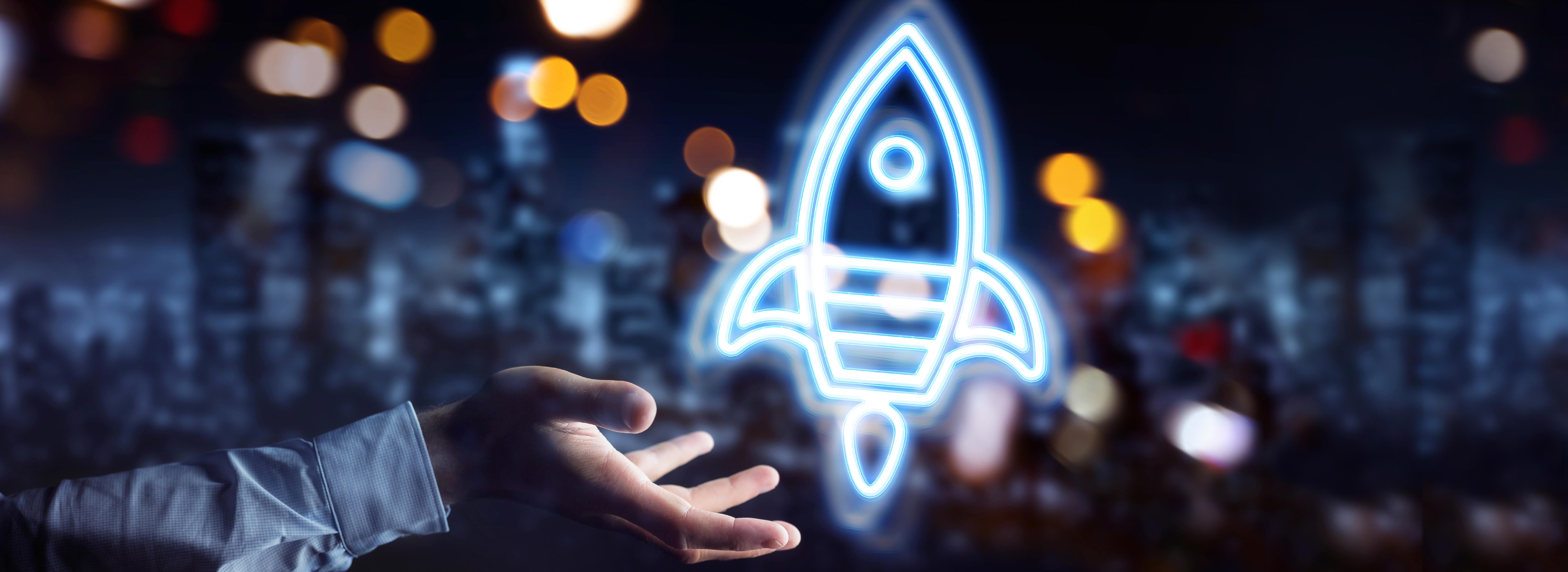 Eine Hand streckt sich aus, während darüber eine leuchtende, stilisierte Rakete schwebt. Der Hintergrund ist verschwommen, mit unscharfen Lichtern, die eine dynamische, futuristische Atmosphäre schaffen. Das Bild vermittelt das Gefühl von Aufbruch und Innovation.